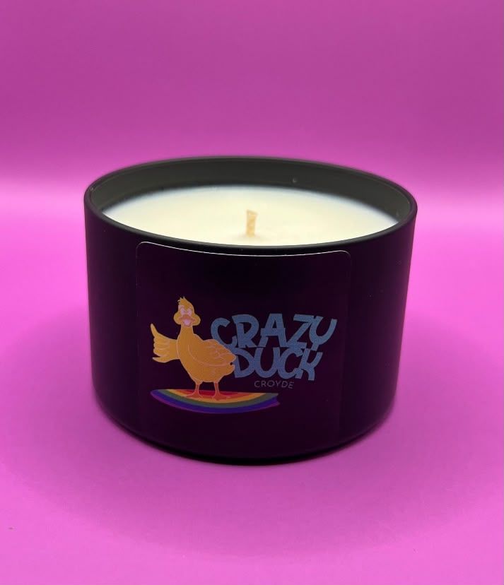 A Crazy Duck 8oz soy candle in a matte black tin with the duck-on-a-surfboard label