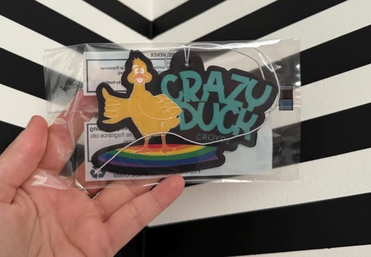 A Crazy Duck car air freshener in its packaging: the duck on a rainbow surfboard