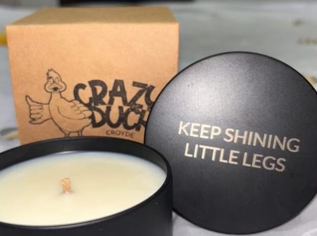 An engraved lid reading Keep shining little legs, beside a candle and a kraft Crazy Duck gift box